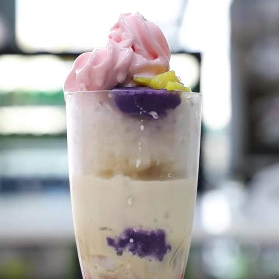 Halo-halo in a tall footed glass topped with a pale pink ice cream swirl, purple ube halaya and yellow jackfruit strips over shaved ice and a creamy milk layer at Pinoy Tambayan