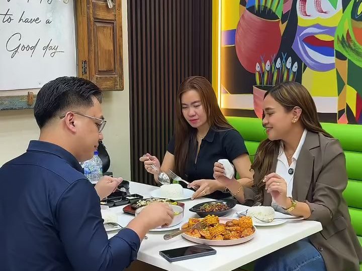 Three diners sharing rice, a sizzling plate and a platter of prawns under the mural in Al Barsha