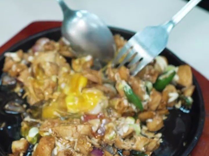 Sizzling chicken sisig topped with a fried egg on a hot plate at Pinoy Tambayan