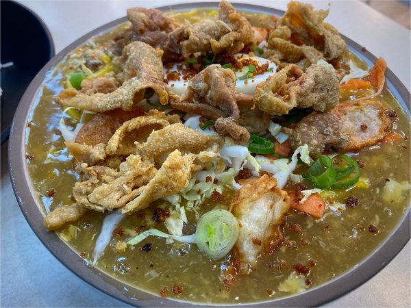 Bowl of pancit palabok buried under crispy chicharon, shredded cabbage, carrot, spring onion and a boiled egg
