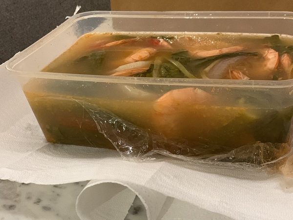 Takeaway tub of sinigang na hipon, prawns in sour tamarind broth with kangkong, beside a paper bag and a Pinoy Tambayan card