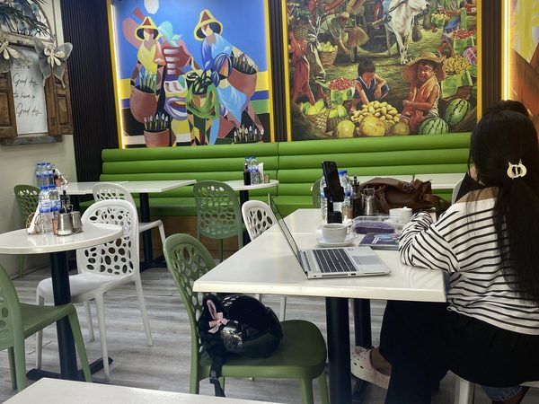 Bright dining room with Philippine murals, green banquettes and white tables, with a customer working at a laptop