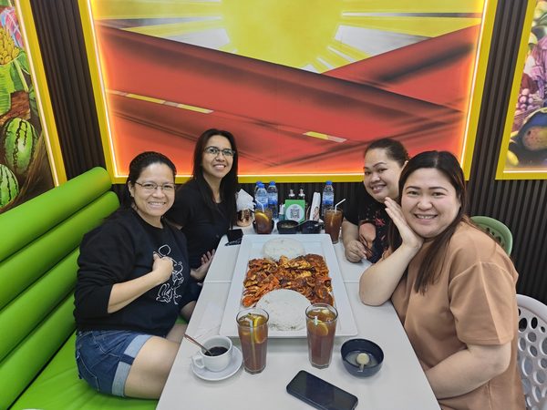 Four women smiling at the camera around a long platter of chilli crab and garlic rice with iced tea