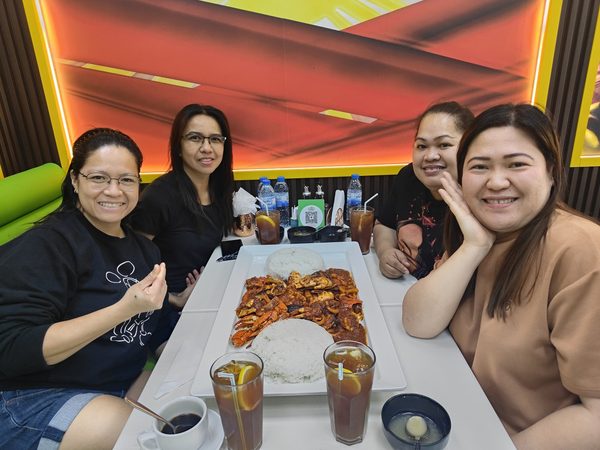 Group of four women posing at their table with a chilli crab and rice platter in front of the Philippine flag mural