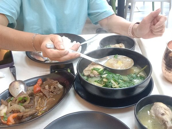 Table of bulalo soup, sizzling beef with onions and peppers, tinolang manok and steamed rice, with a diner seated behind