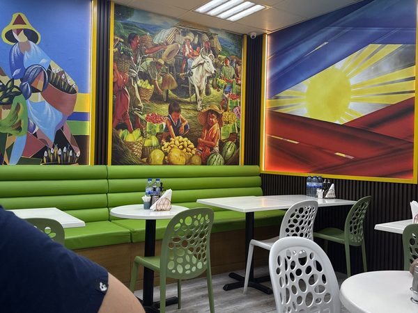 Dining area with green banquette seating, white tables and three large murals including the Philippine flag sun and rays