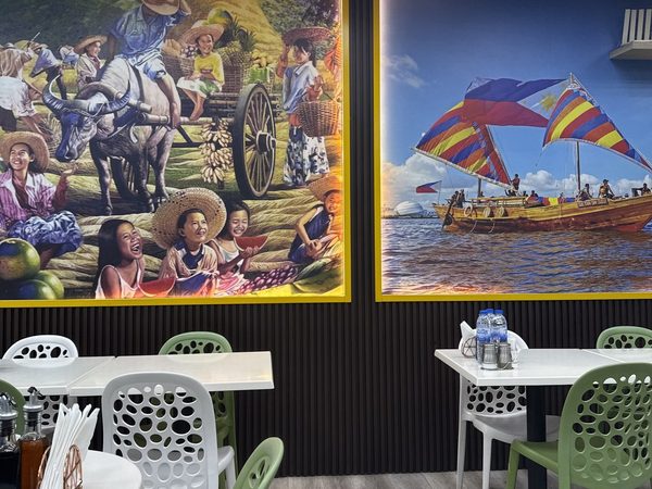 Empty dining tables and green chairs beneath murals of a Philippine harvest scene and a colourful sailing vinta