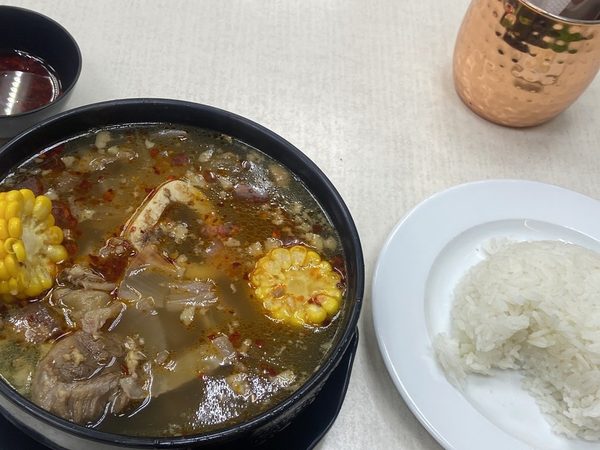 Bulalo beef shank soup with sweet corn in a black pot, with a side plate of steamed rice and a small bowl of the broth