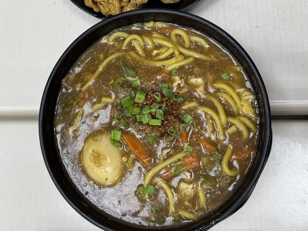 Pancit lomi thick noodle soup with boiled egg, carrots, spring onion and fried garlic, with a plate of chicharon and a tray of chilli oil, soy dip and lemon