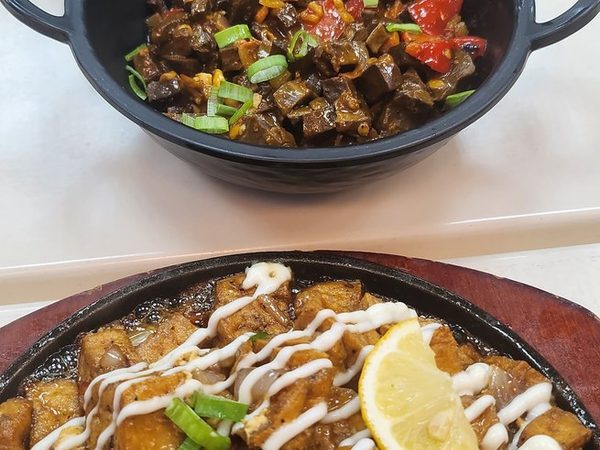 Sizzling sisig drizzled with mayonnaise and topped with spring onion and lemon, with a bowl of chopped meat in chilli and a dish of prawns in coconut cream