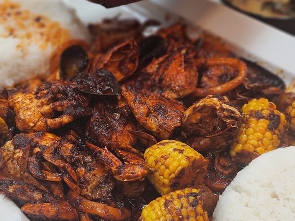 A large seafood platter of crab, prawns, squid rings and corn with rice, as a sizzling plate of sisig is held above it