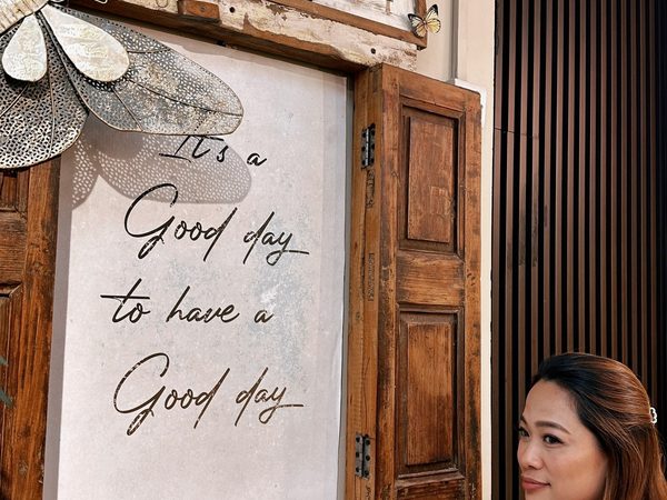 A woman standing beside the rustic wooden wall sign reading It's a Good day to have a Good day in the dining room
