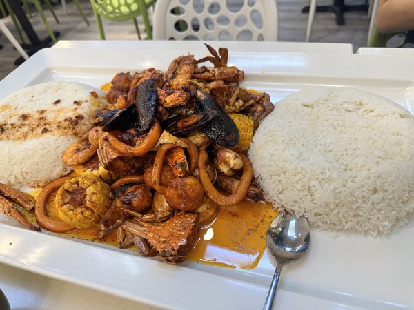 A seafood boodle platter of crab, prawns, squid rings, mussels, sausage and corn in sauce, flanked by two mounds of steamed rice