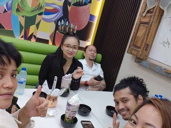Five adult diners at a table with ube halo halo in tall glasses, in front of the restaurant's bright Filipino mural