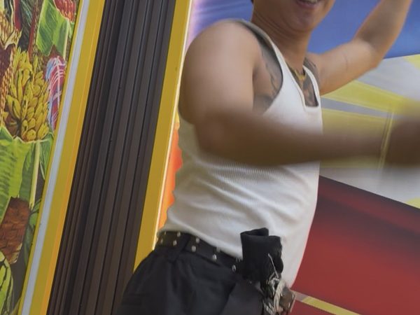 A man in a white tank top, flat cap and sunglasses posing with his arm raised beside the restaurant's painted Filipino wall art