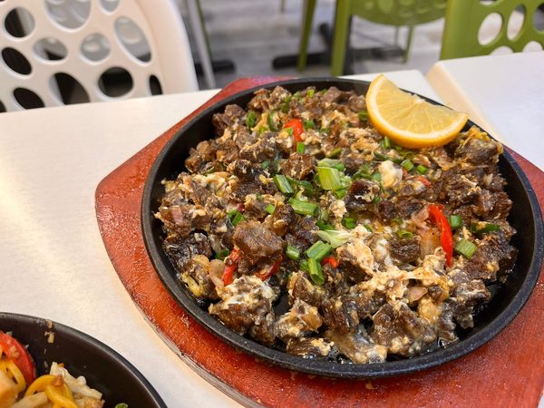 Sizzling beef sisig with egg, spring onion, red chilli and a lemon wedge on a cast iron plate