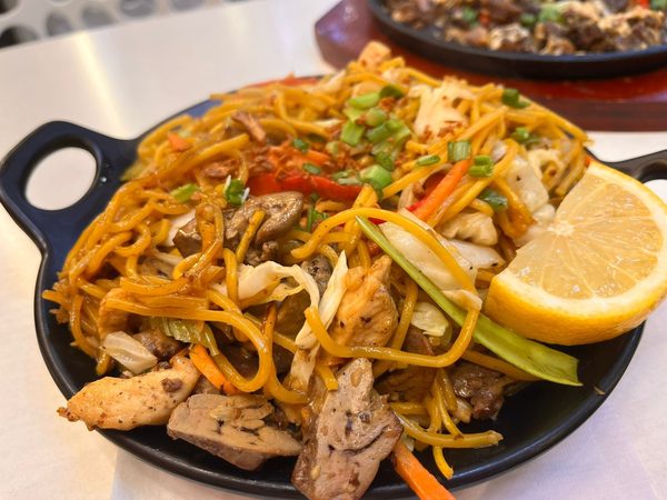 Pancit canton with chicken, mushrooms, cabbage and carrots served with a lemon wedge on a black skillet plate