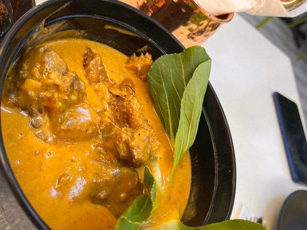 A bowl of kare kare, oxtail and beef in thick peanut sauce garnished with fresh bok choy leaves