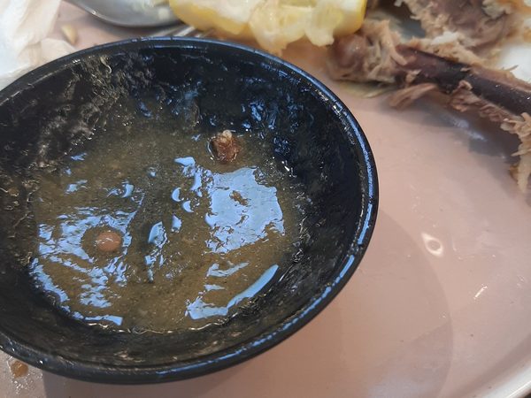 An emptied black dipping sauce bowl beside picked over crispy pata bones and lemon on a plate