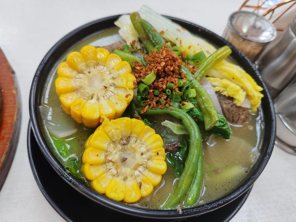 A bowl of bulalo, beef shank soup with sweetcorn, string beans, bok choy and cabbage in a clear broth topped with fried garlic