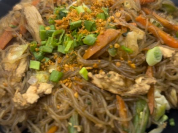 Plate of pancit bihon noodles with sliced chicken, carrots, cabbage, spring onions and toasted garlic on a black dish.