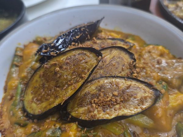 Bowl of creamy coconut squash and eggplant vegetable stew with string beans, topped with fried garlic and served with a plate of steamed rice.