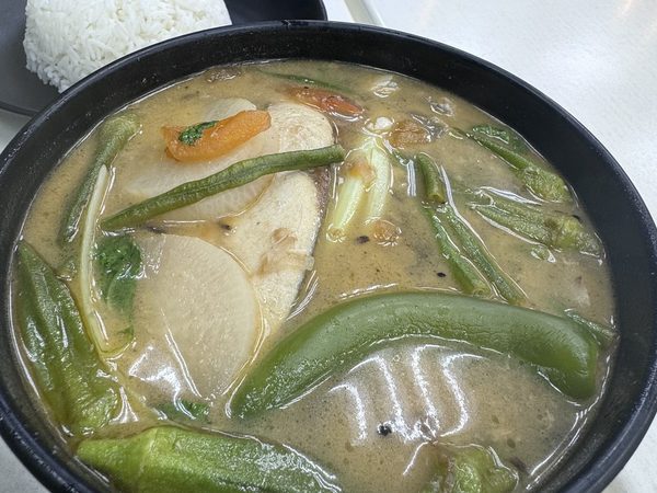 Bowl of sinigang na isda, sour tamarind fish soup with radish, okra, string beans, tomato and green chilli, beside a plate of steamed rice.