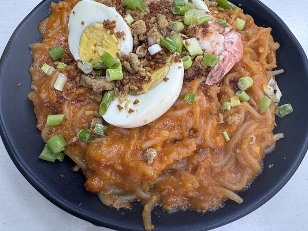 Pancit palabok topped with prawns, halved hard-boiled egg, crushed chicharon, spring onions and a lemon wedge.