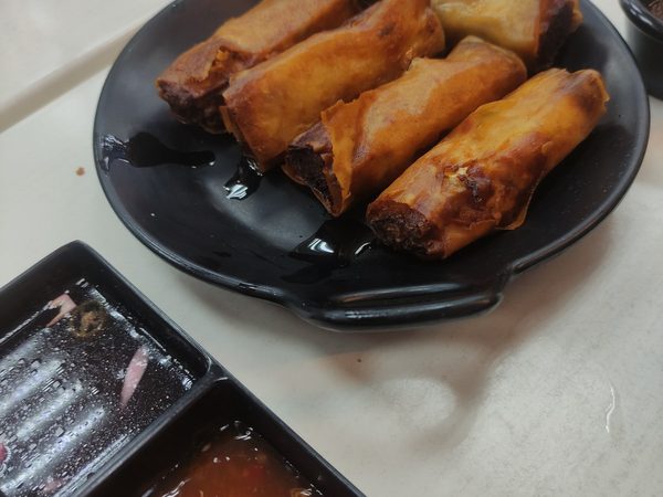 Fried lumpia spring rolls on a black plate served with sweet chilli sauce and a vinegar and onion dip.