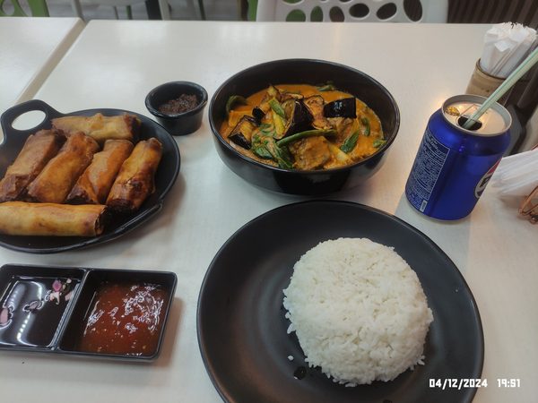 Table spread of fried lumpia, kare kare with bagoong, a mound of steamed rice, dipping sauces and a chilled soft drink.