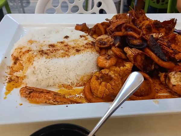 Seafood boodle platter on a long white tray with crab, prawns, squid rings, clams, corn and garlic rice in a spiced butter sauce.