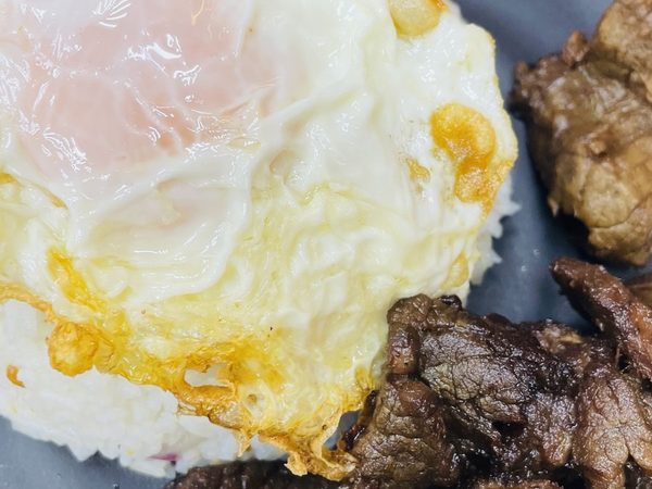 Tapsilog on a black plate with sweet beef tapa, steamed rice and a sunny-side-up fried egg.