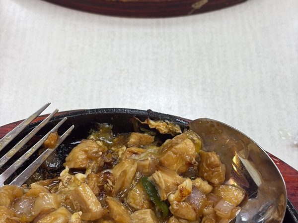 Two servings of sizzling chicken sisig with steamed rice on cast iron plates set into wooden boards.