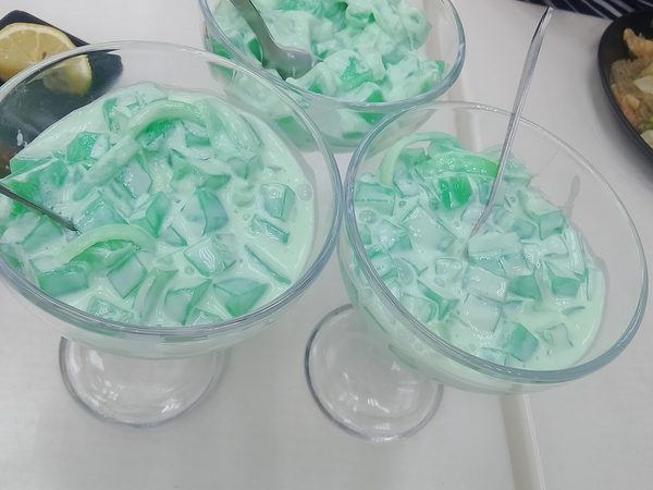 Three tall glasses of buko pandan, pale green jelly cubes and young coconut strips in sweetened cream.