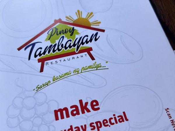 Pinoy Tambayan Restaurant menu card on a dark wooden table, showing the house logo and the tagline Sarap kasama ng pamilya.