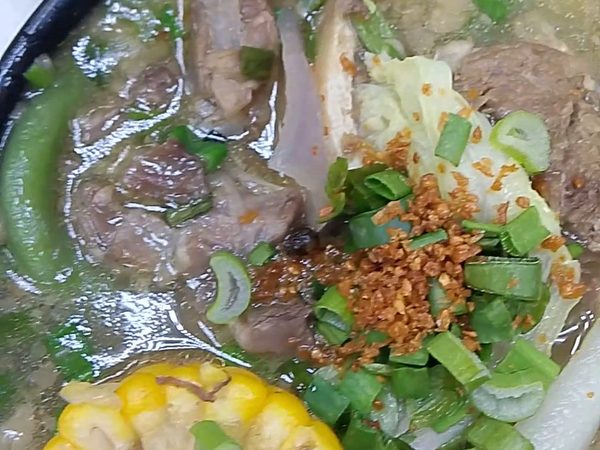 Close-up of bulalo beef shank soup with corn on the cob, radish, cabbage, long beans, spring onions and toasted garlic.
