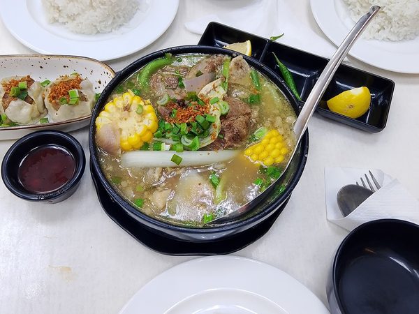 Table set with a large bowl of bulalo beef shank soup, a plate of siomai dumplings and three plates of steamed rice.