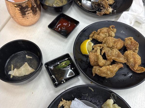Table of part-eaten dishes including crispy fried chicken skin, bowls of soup, dipping sauces and a copper cup.