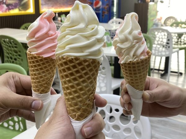 Three hands raising vanilla and strawberry soft serve cones together in the dining room.