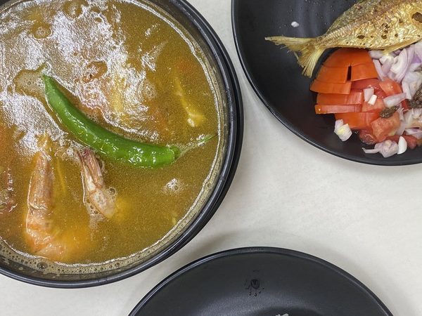 Overhead spread of sinigang na hipon, fried daing fish with tomato and onion salad, grilled longganisa and a plate of steamed rice.