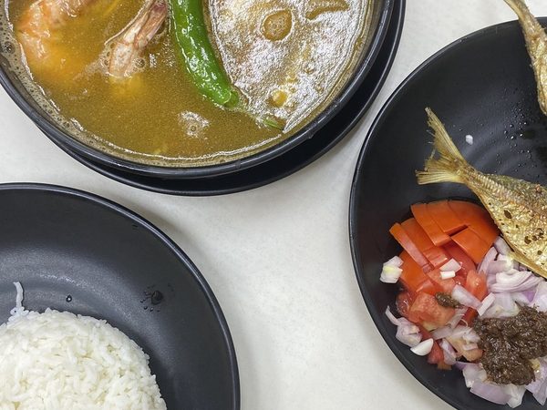 Bowl of sinigang na hipon with a green chilli beside fried fish, tomato and onion salad with bagoong, and a plate of steamed rice.