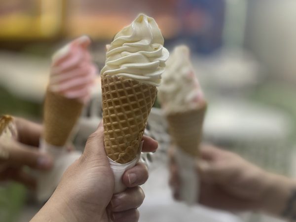 Close-up of a hand holding a vanilla soft serve cone with two more cones blurred behind it.