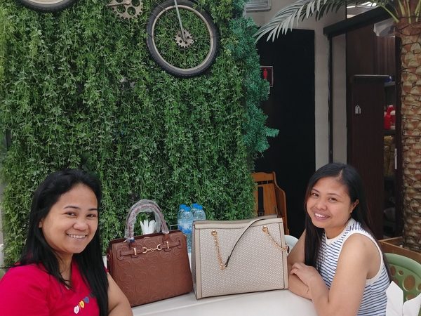 Two women seated at a table with bowls of soup in front of a green foliage wall decorated with a bicycle and a vintage clock.