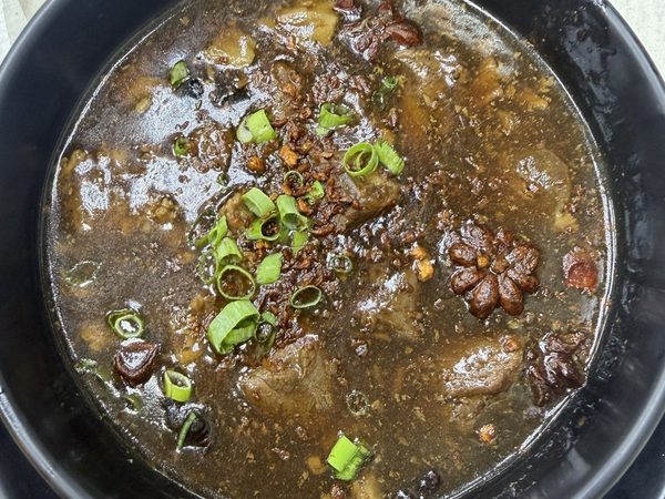 Bowl of beef pares stew in dark star anise broth topped with fried garlic and sliced spring onion.