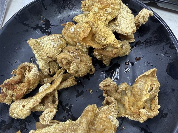 Plate of crispy golden fried pork chicharon with soy vinegar and ketchup dips alongside.