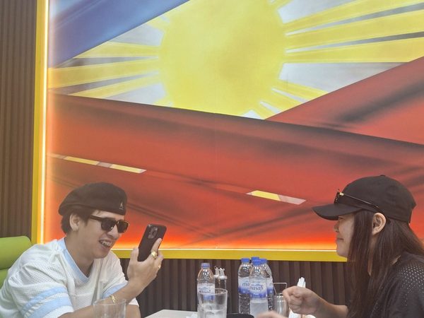 Two adult diners laughing at a table in front of the restaurant's large Philippine flag mural, with soup bowls and water bottles on the table.