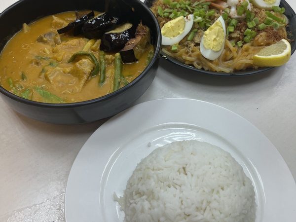 Bowl of kare kare with eggplant, string beans and pechay in peanut sauce, a plate of pancit palabok topped with sliced boiled egg, shrimp and crushed chicharon, and a plate of steamed rice.