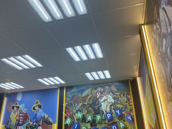 Restaurant interior looking up at the ceiling lights, painted Filipino market murals and a Happy Birthday banner above green booth seating