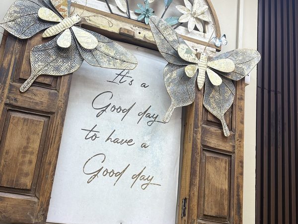 Restaurant wall decor made from a reclaimed wooden window frame with large metal butterflies, flowers and a sign reading It's a Good day to have a Good day.