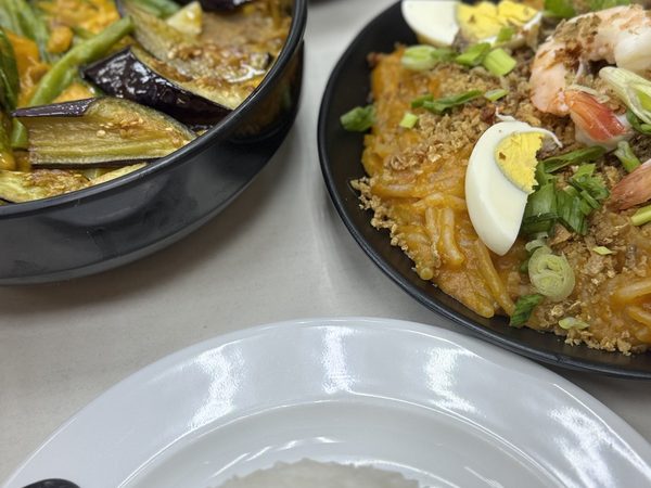 Pinakbet of eggplant and string beans in squash sauce beside pancit palabok topped with boiled egg, prawns, crushed chicharron and spring onion, with a plate of steamed rice